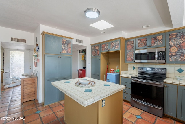 2621 W Rapallo Way, Tucson, AZ 85741 - kitchen featuring stainless steel microwave, range with electric stovetop, tile countertops, a skylight, and decorative backsplash
