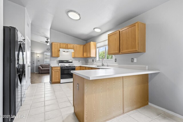 8807 S Desert Rainbow Dr, Tucson, AZ 85747 - kitchen with white range, black fridge, a sink, under cabinet range hood, and a peninsula