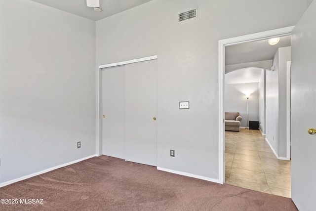 8807 S Desert Rainbow Dr, Tucson, AZ 85747 - unfurnished bedroom with arched walkways, carpet floors, a closet, baseboards, and tile patterned floors
