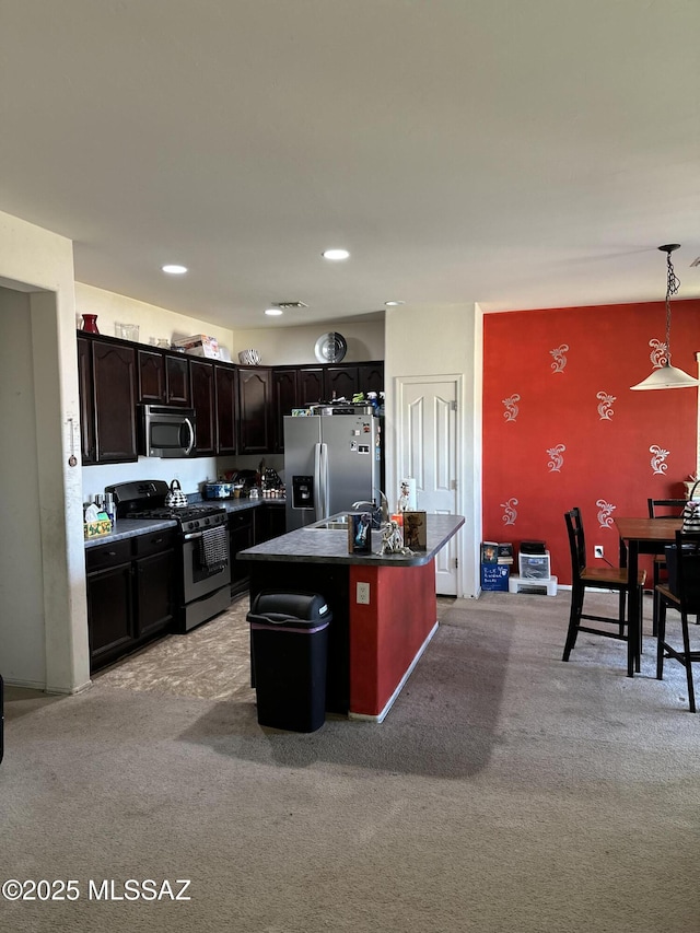 1027 E Madera Grove Ln, Sahuarita, AZ 85629 - kitchen featuring appliances with stainless steel finishes, decorative light fixtures, light colored carpet, dark countertops, and a kitchen island with sink