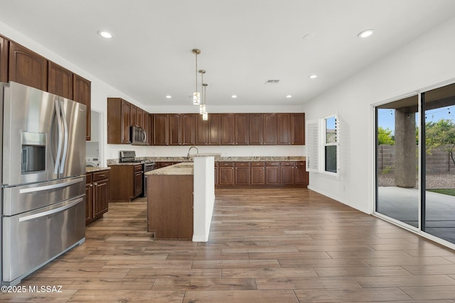 kitchen featuring stainless steel appliances, recessed lighting, wood finished floors, a sink, and an island with sink