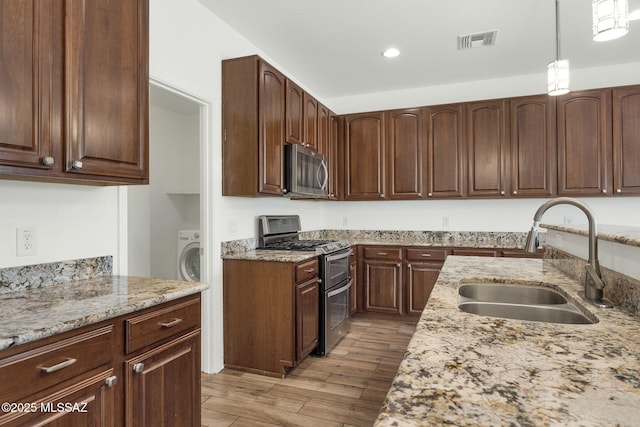 kitchen with appliances with stainless steel finishes, a sink, light stone countertops, light wood-type flooring, and hanging light fixtures