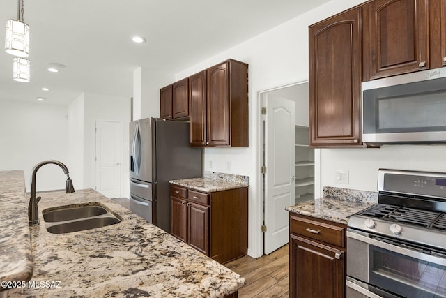 kitchen featuring appliances with stainless steel finishes, a sink, light wood finished floors, light stone countertops, and decorative light fixtures