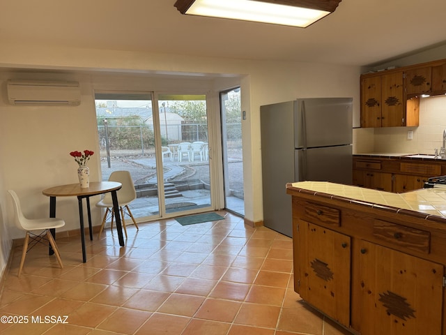 4910 N Gold Ave, Tucson, AZ 85705 - kitchen featuring a wall mounted AC, tile counters, freestanding refrigerator, brown cabinetry, and tasteful backsplash