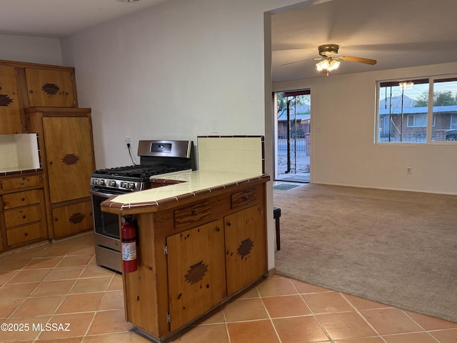 4910 N Gold Ave, Tucson, AZ 85705 - kitchen with gas range, tile counters, brown cabinets, light tile patterned floors, and light carpet