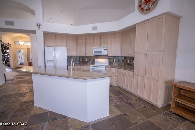 4416 N Saddle View Dr, Tucson, AZ 85750 - kitchen featuring white appliances, stone tile flooring, arched walkways, a center island with sink, and decorative backsplash