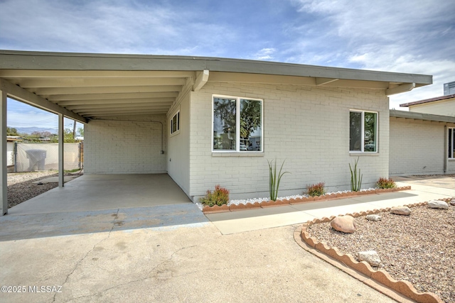 view of front of house with brick siding, an attached carport, fence, and driveway