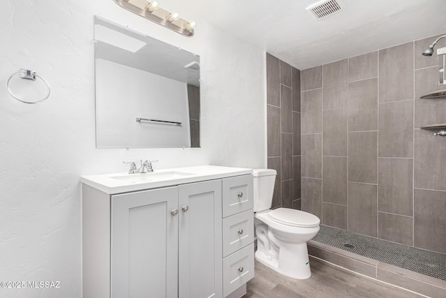 bathroom with tiled shower, wood finished floors, vanity, and toilet