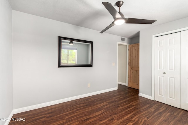 unfurnished bedroom with dark wood-type flooring, baseboards, a closet, and a ceiling fan