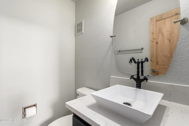 bathroom with toilet, a textured wall, and vanity