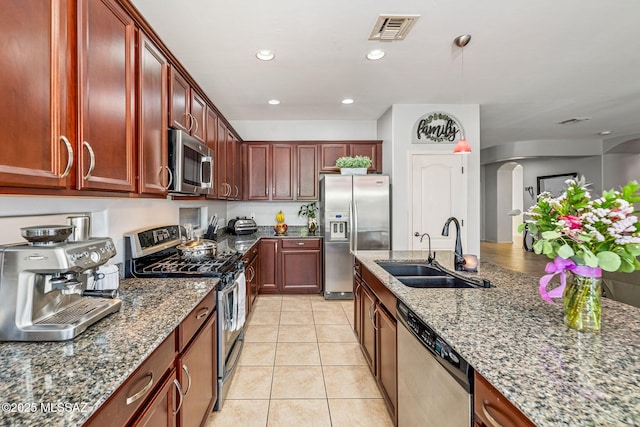 832 E Grosvener Hills Pl, Sahuarita, AZ 85629 - kitchen with stainless steel appliances, a sink, arched walkways, dark stone counters, and light tile patterned flooring