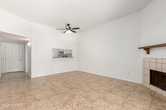 7244 S Camino Del Arco Iris, Tucson, AZ 85746 - unfurnished living room featuring a ceiling fan, a tiled fireplace, and high vaulted ceiling