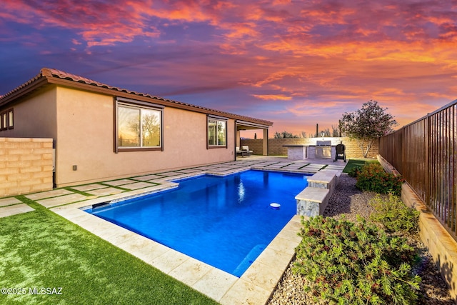 7106 W Foothills Acacia Pl, Marana, AZ 85658 - pool at dusk with exterior kitchen, a fenced backyard, and a patio