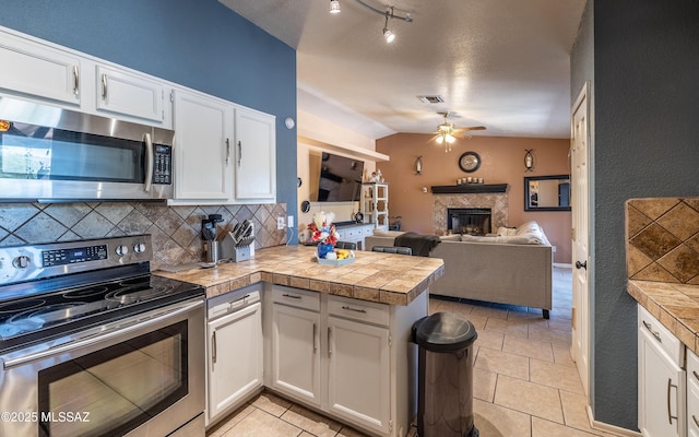 253 Grillo Ct, Rio Rico, AZ 85648 - kitchen with appliances with stainless steel finishes, a peninsula, a ceiling fan, a fireplace, and white cabinetry
