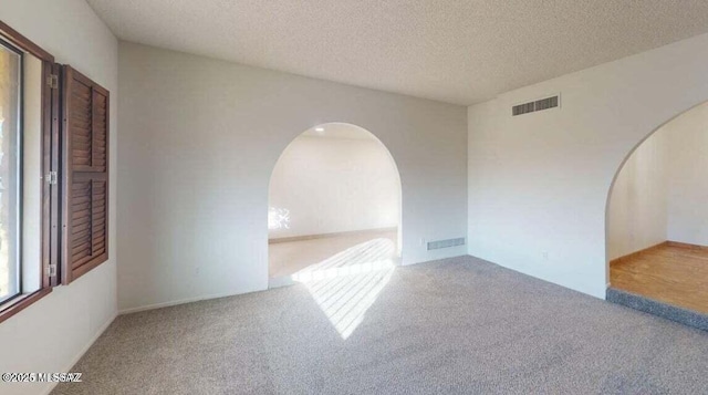 carpeted spare room featuring arched walkways and a textured ceiling