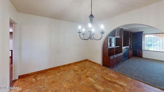 unfurnished dining area with a chandelier, arched walkways, and a textured ceiling