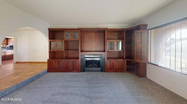 unfurnished living room featuring carpet floors, a fireplace, arched walkways, and a textured ceiling