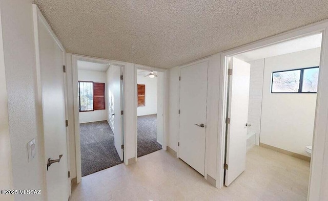 hall with a textured ceiling and baseboards