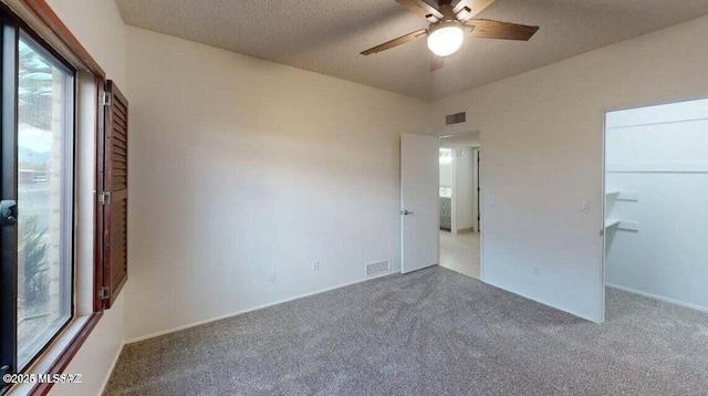 unfurnished bedroom featuring carpet flooring, multiple windows, a ceiling fan, and a textured ceiling