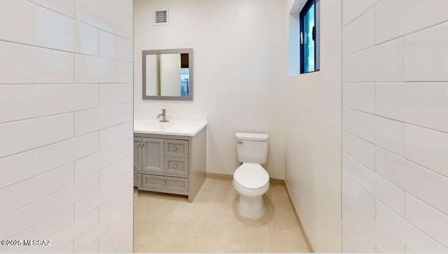 bathroom with toilet, vanity, tile patterned floors, baseboards, and tile walls