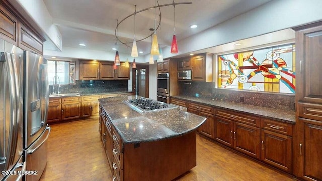 kitchen featuring stainless steel appliances, a kitchen island, wood finished floors, decorative backsplash, and dark stone counters