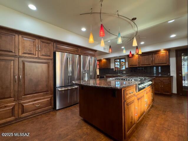 kitchen featuring stainless steel fridge with ice dispenser, a kitchen island, gas cooktop, dark stone counters, and tasteful backsplash