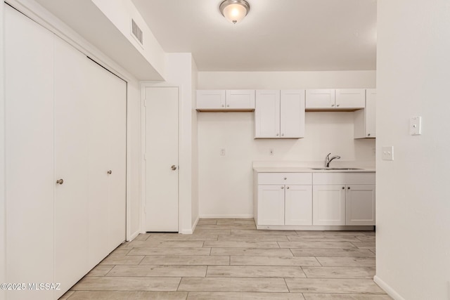 kitchen featuring a sink, light wood finished floors, light countertops, and baseboards