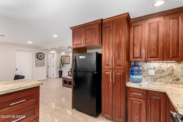kitchen featuring freestanding refrigerator, light stone counters, decorative backsplash, brown cabinetry, and recessed lighting