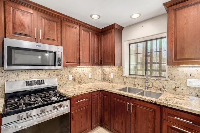 kitchen with appliances with stainless steel finishes, a sink, light stone counters, backsplash, and light tile patterned floors