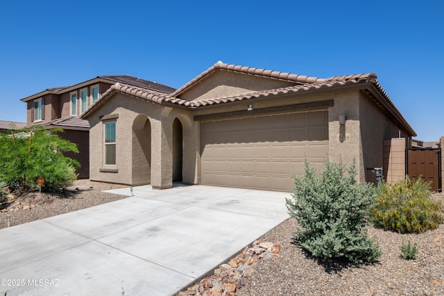 mediterranean / spanish home with an attached garage, stucco siding, driveway, and a tiled roof