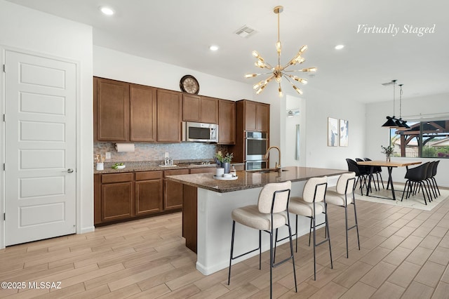 12513 Denton Way, Marana, AZ 85653 - kitchen with stainless steel appliances, a kitchen breakfast bar, light wood-style flooring, decorative light fixtures, and a kitchen island with sink
