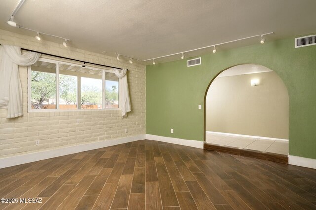 3600 N Hash Knife Cir, Tucson, AZ 85749 - unfurnished room with track lighting, baseboards, brick wall, arched walkways, and wood finished floors