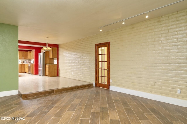 3600 N Hash Knife Cir, Tucson, AZ 85749 - spare room featuring baseboards, track lighting, a chandelier, wood finished floors, and brick wall
