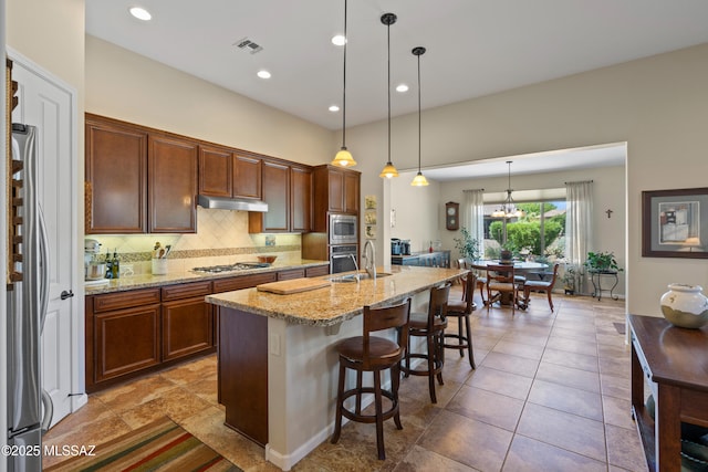 59962 E Arroyo Grande Dr, Oracle, AZ 85623 - kitchen with stainless steel appliances, a sink, under cabinet range hood, a breakfast bar area, and light stone countertops