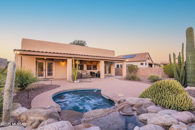 8183 N Sombrero Point Dr, Tucson, AZ 85743 - back of property at dusk featuring french doors, a patio, stucco siding, an in-ground hot tub, and a tiled roof