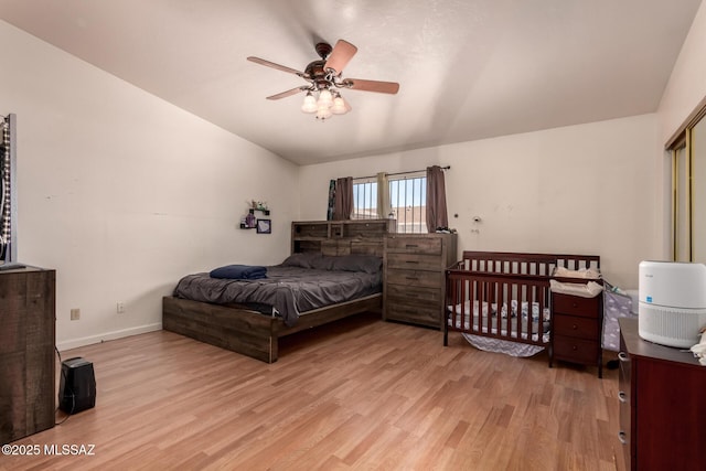 bedroom with light wood-type flooring, vaulted ceiling, baseboards, and a ceiling fan