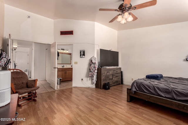 bedroom featuring light wood-style floors, vaulted ceiling, connected bathroom, a ceiling fan, and baseboards