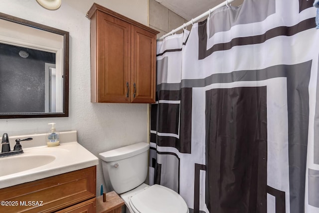 bathroom with toilet, vanity, a textured wall, and a shower with curtain