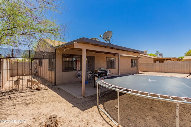 back of property with stucco siding, a trampoline, a fenced backyard, and a patio area