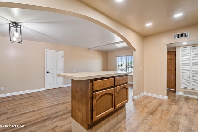 2002 E Pinon Dr, Tucson, AZ 85706 - kitchen featuring light wood finished floors, arched walkways, baseboards, light countertops, and brown cabinetry