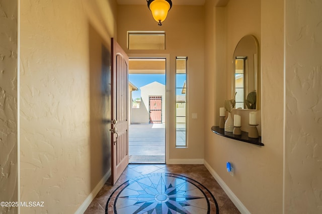 13715 N Tessali Way, Tucson, AZ 85755 - doorway to outside with baseboards, inlaid floor details, a textured wall, and arched walkways