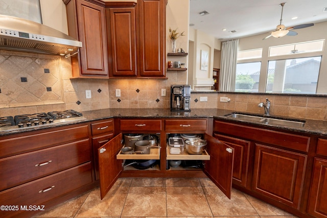 13715 N Tessali Way, Tucson, AZ 85755 - kitchen with wall chimney range hood, a sink, stainless steel gas stovetop, ceiling fan, and dark stone counters