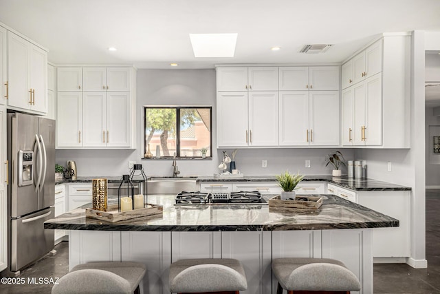9840 N Desert Sky Rd, Tucson, AZ 85737 - kitchen with stainless steel appliances, a breakfast bar area, white cabinets, a skylight, and dark stone counters