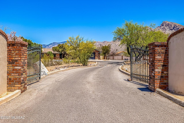 9840 N Desert Sky Rd, Tucson, AZ 85737 - view of asphalt road with a gate, a mountain view, and curbs