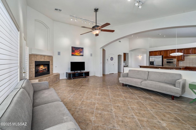 1048 E Rodda River Pl, Tucson, AZ 85718 - living room with a tiled fireplace, a ceiling fan, track lighting, arched walkways, and a towering ceiling