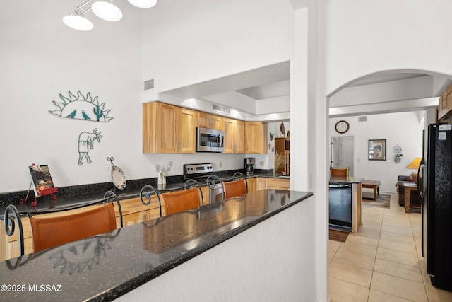 7133 E Grey Fox Ln, Tucson, AZ 85750 - kitchen featuring appliances with stainless steel finishes, arched walkways, light tile patterned floors, and dark stone counters