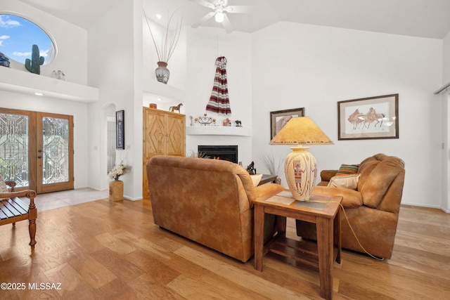 7133 E Grey Fox Ln, Tucson, AZ 85750 - living room featuring a ceiling fan, light wood finished floors, high vaulted ceiling, a lit fireplace, and french doors