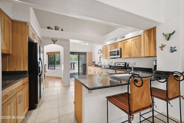 7133 E Grey Fox Ln, Tucson, AZ 85750 - kitchen featuring appliances with stainless steel finishes, a peninsula, light tile patterned floors, a kitchen bar, and arched walkways