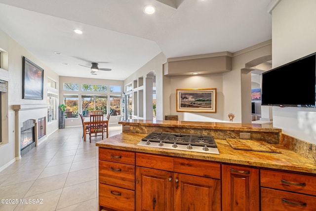 1861 E Crown Ridge Way, Oro Valley, AZ 85755 - kitchen featuring stainless steel gas stovetop, ceiling fan, a glass covered fireplace, light stone counters, and light tile patterned floors