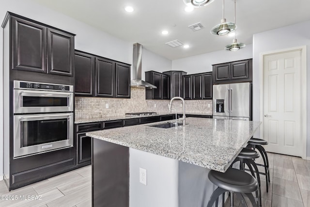 11874 N Raphael Way, Tucson, AZ 85742 - kitchen featuring stainless steel appliances, wall chimney exhaust hood, a sink, a breakfast bar, and light stone countertops